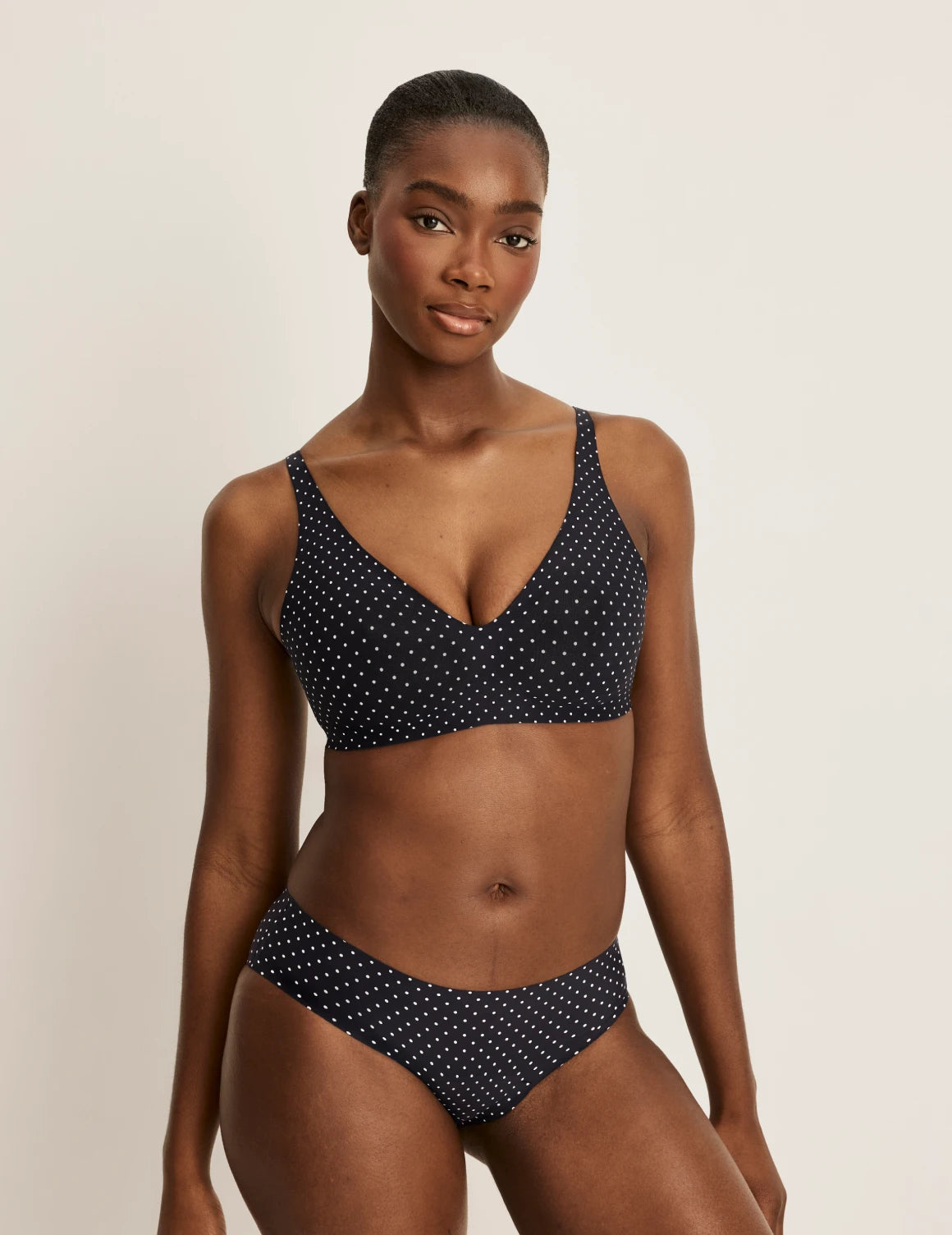 Orlane is a 32DD and wearing KNIX S+ | Full-body of model wearing the Revolution V-Neck Bra, highlighting the neckline, strap design, and smooth silhouette | Black with White Polka Dot